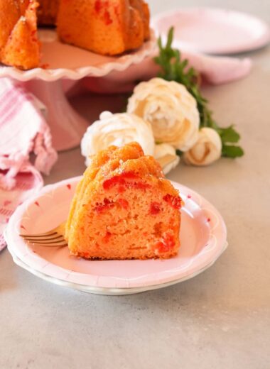 Cherry cake slice on pink plate with flowers, and whole cake in the background.