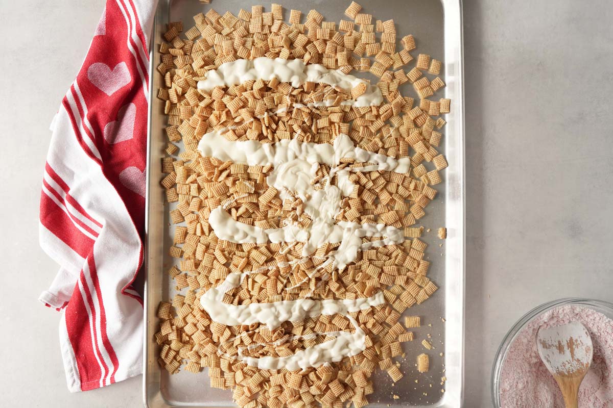 Melted almond bark on rice cereal on a silver baking sheet with a red, striped napkin nearby.