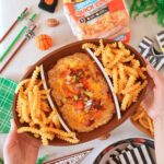 A hand holding up a football platter of cheeseburger dip.