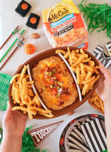 A hand holding up a football platter of cheeseburger dip.