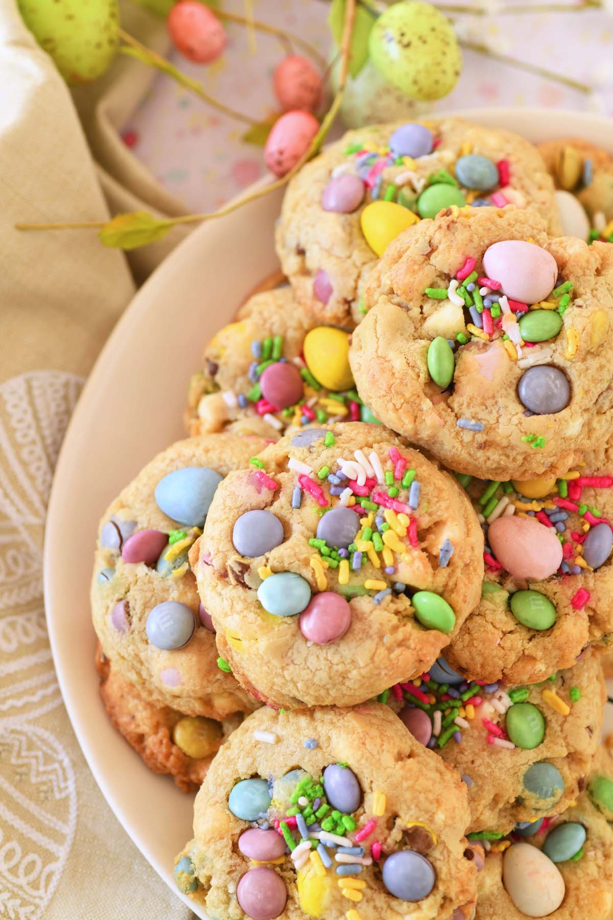 Up-close plate of Easter candy cookies near a tan egg napkin, and pastel Easter egg greenery.
