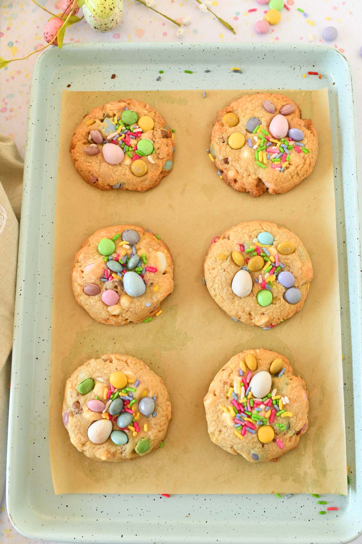 Baked Easter egg cookies on a parchment-lined blue baking sheet.