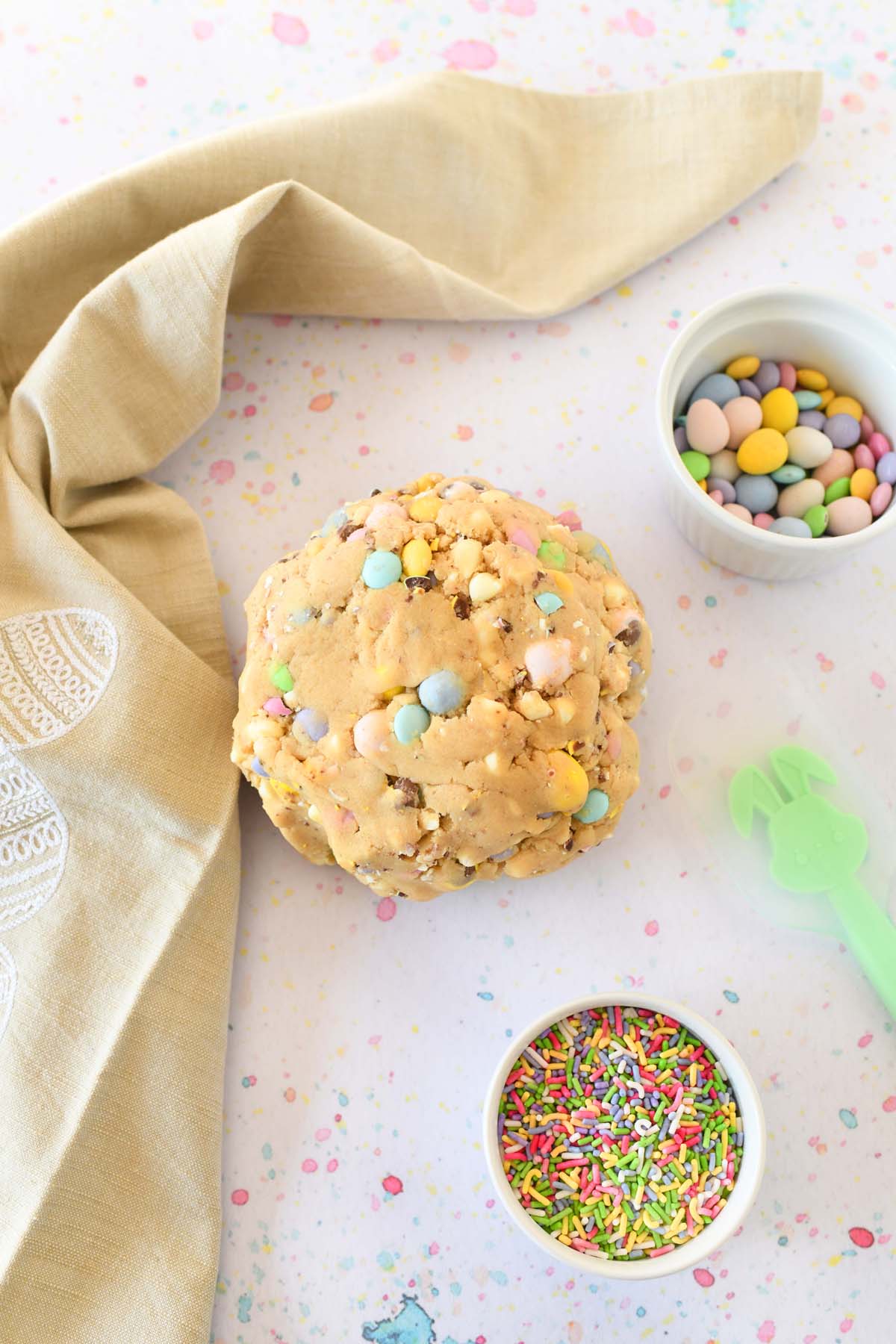 Easter white chocolate chip candy cookie dough ball on a speckled table with a tan egg napkin.