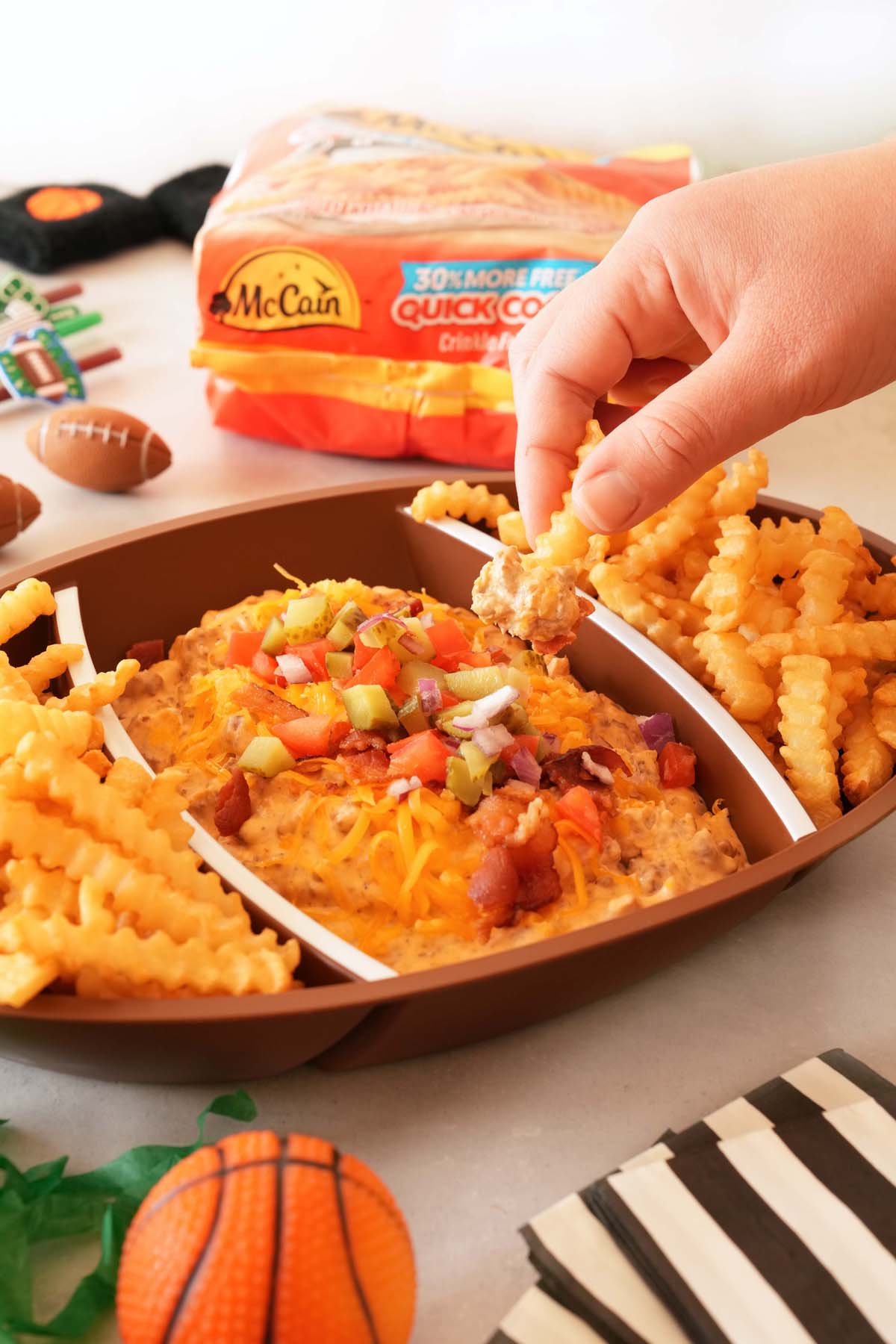 A white hand dipping into cheeseburger dip with a french fry.