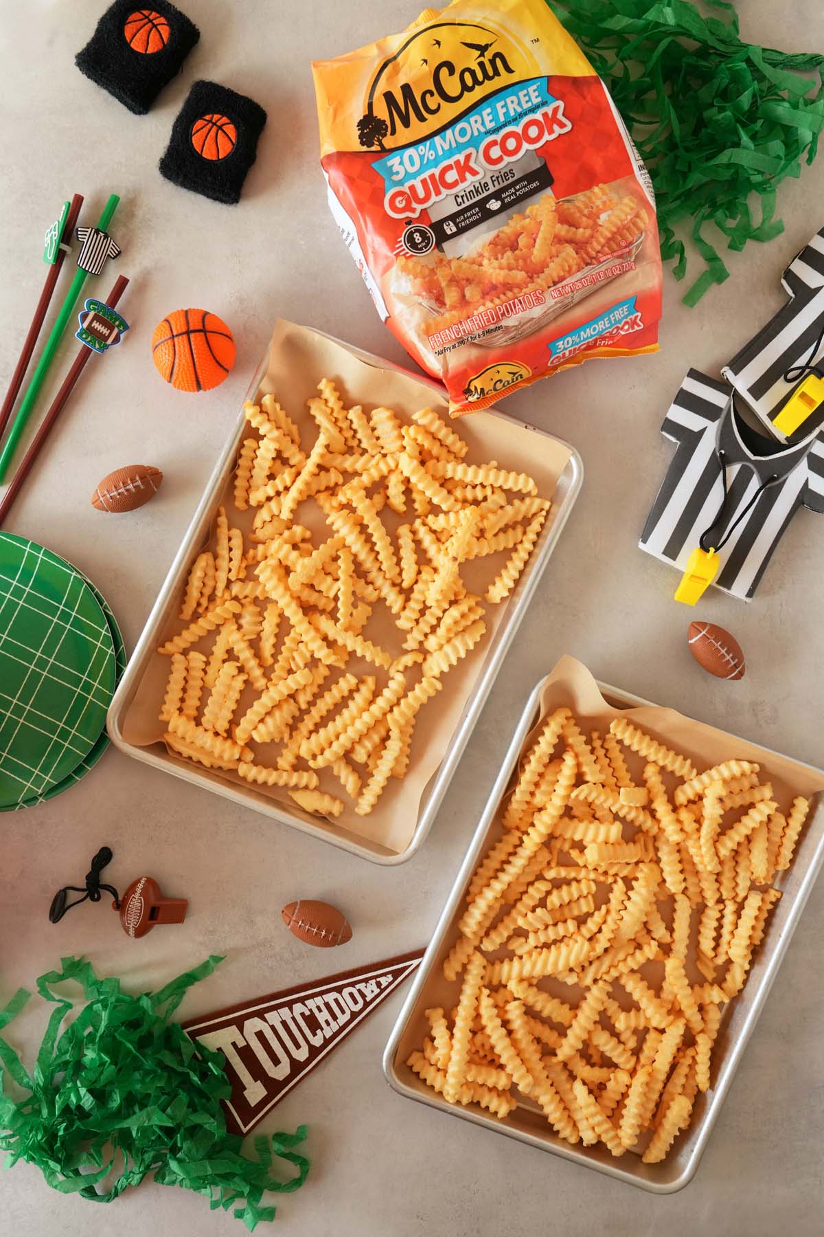 Two pans of McCain Crinkle Cut Fries on a sports themed table.