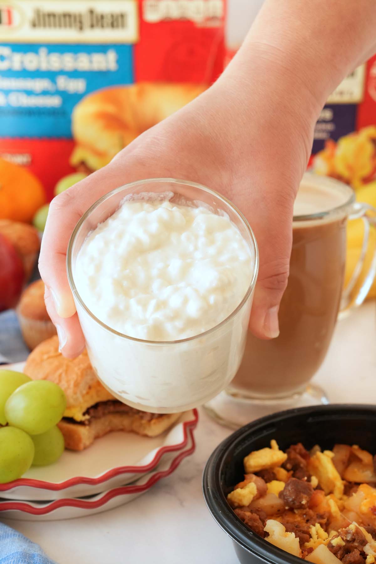 A cup of cottage cheese in a hand near other breakfast foods.