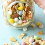 A clear glass jar filled with bunny bait with some spilled onto a blue table.