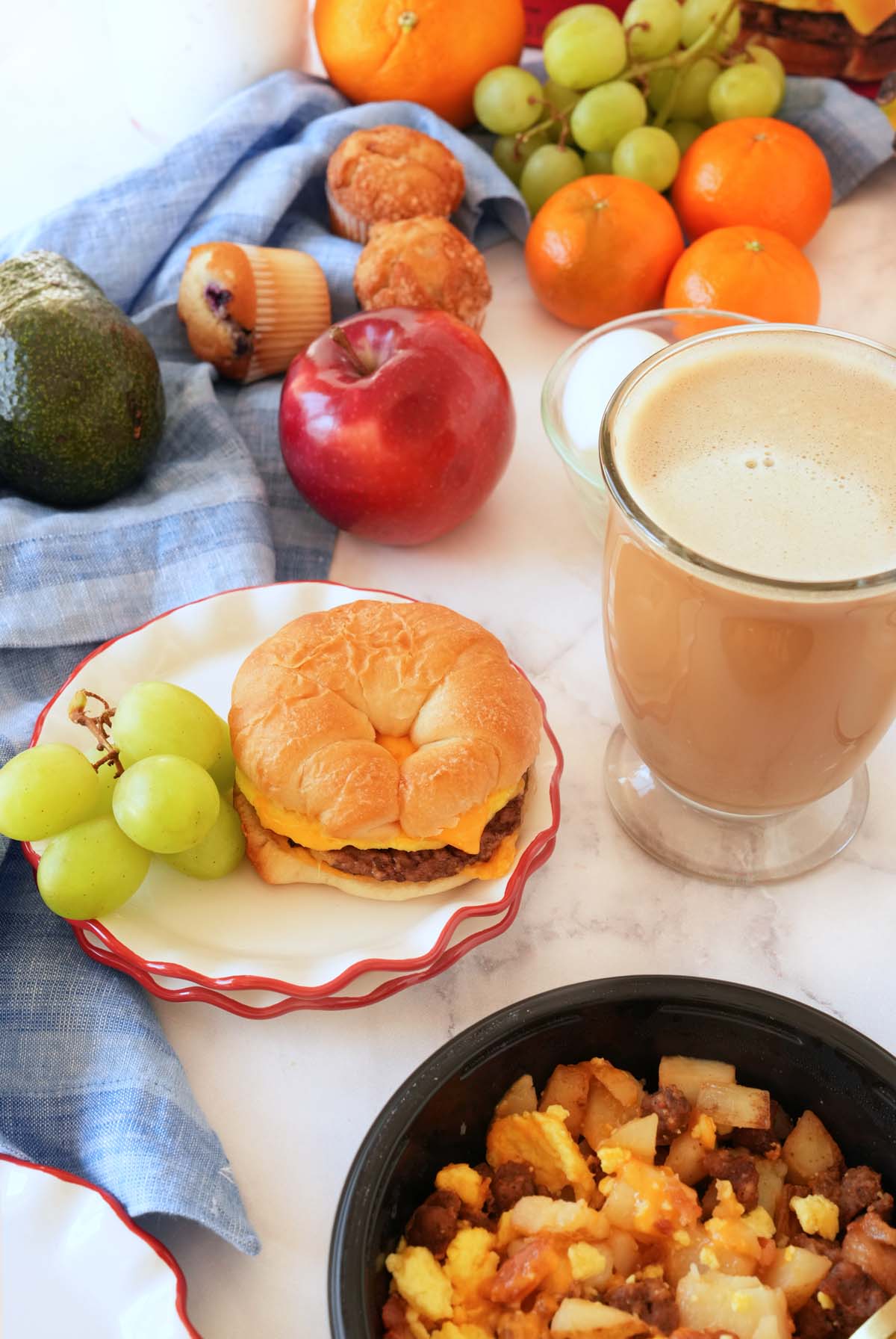A breakfast brunch setting with items from Jimmy Dean plated, fresh fruits, and a coffee on a white table with a blue napkin.