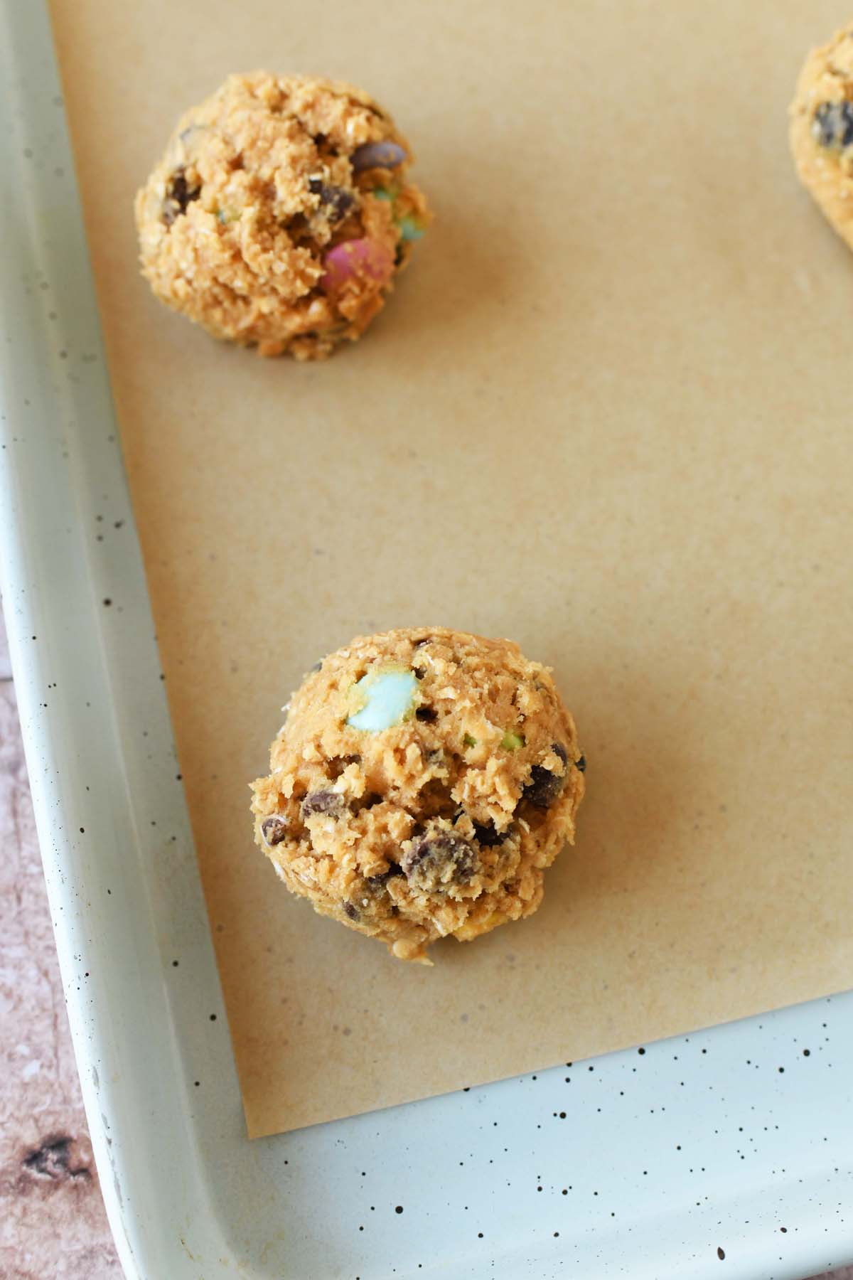 Monster cookie dough ball on a parchment-lined baking sheet.