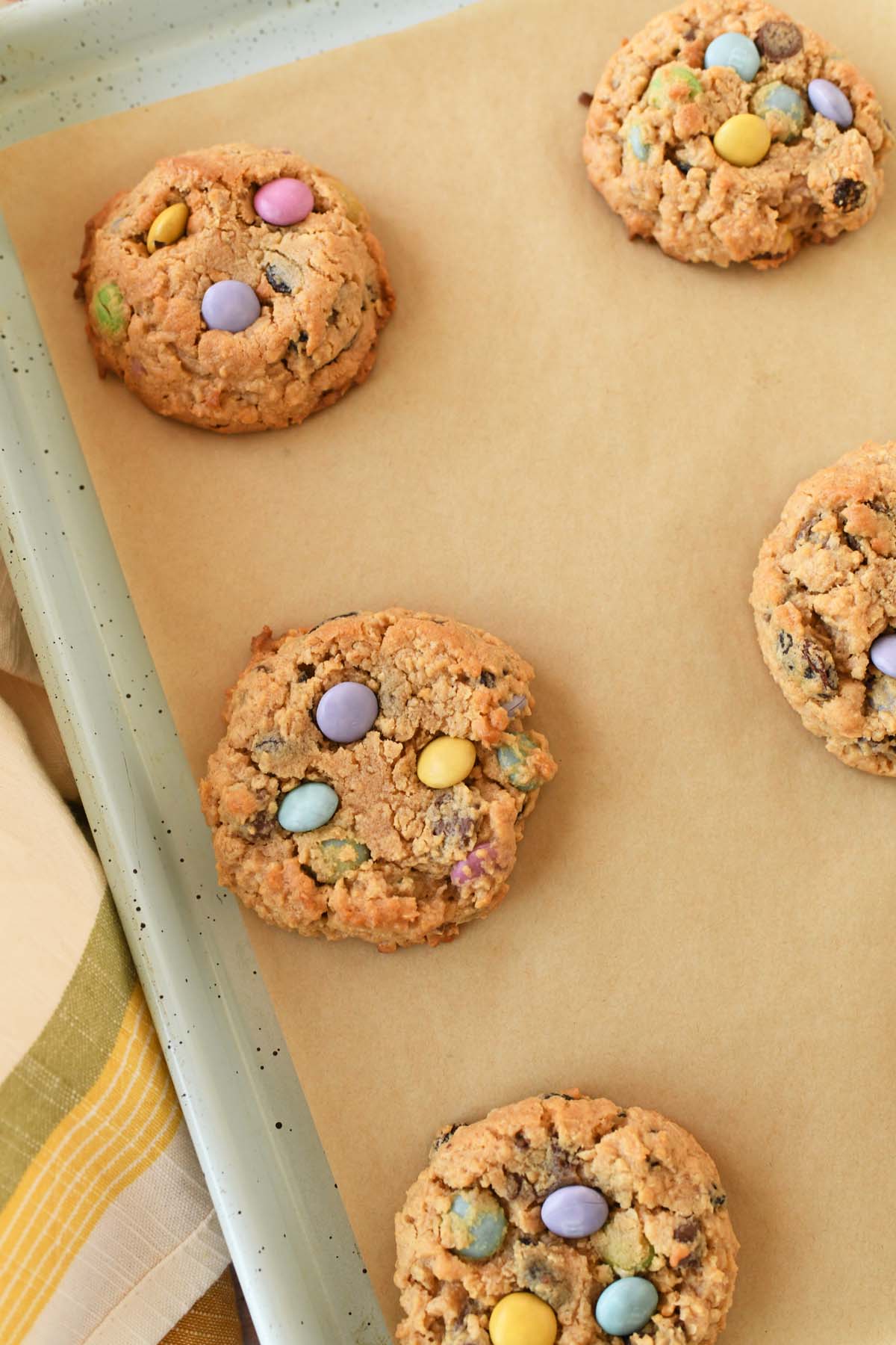 Pastel monster cookies on a parchment-lined blue baking sheet.