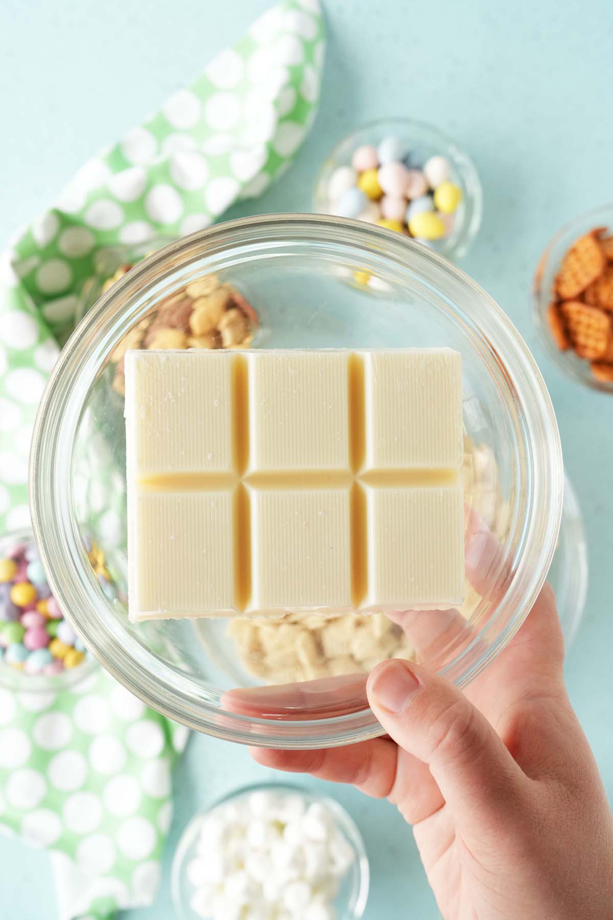 A hand holding up a glass bowl with white almond bark inside.