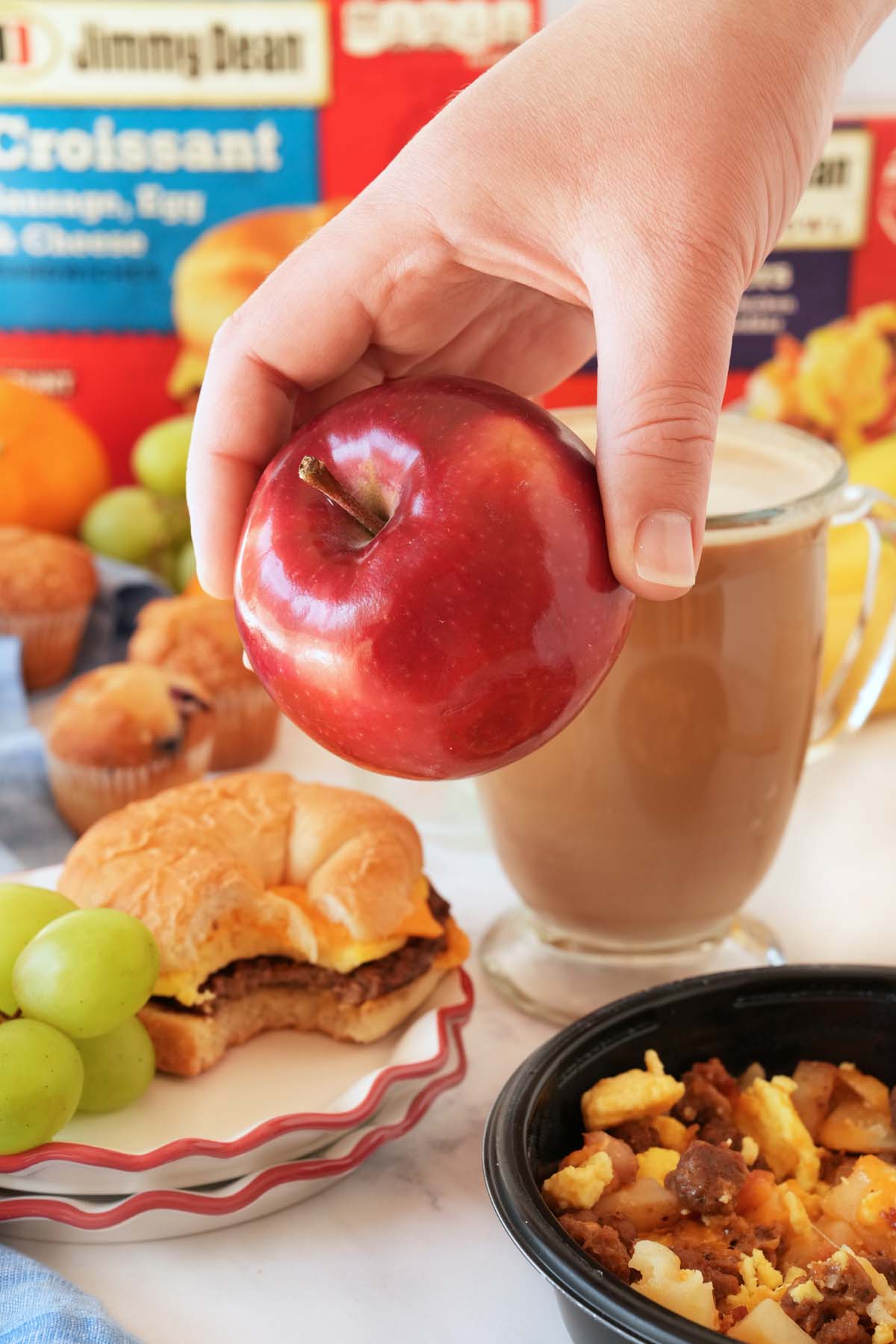 A hand holding a shiny, red apple near a brunch setting.