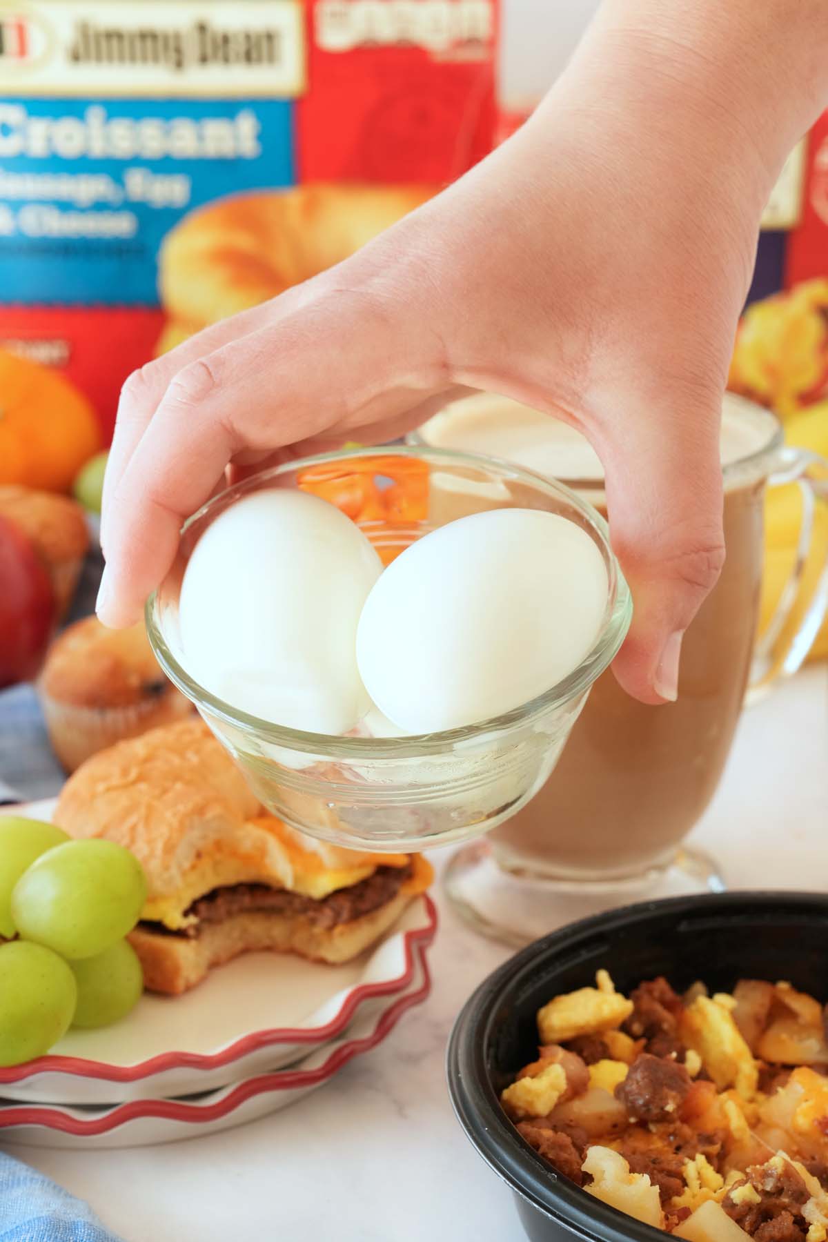 A hand holding a dish of boiled eggs near a brunch setting.