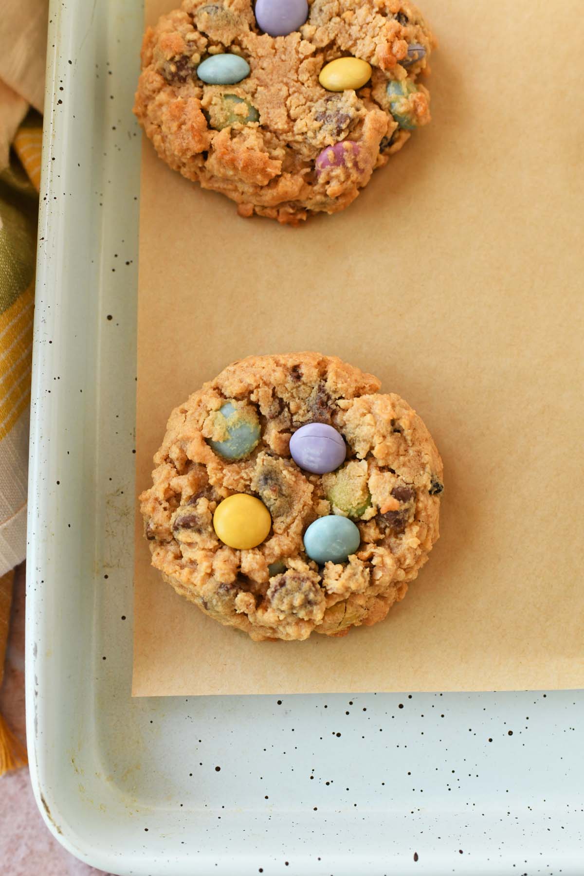 Baked pastel monster cookie on a parchment-lined, blue baking sheet.