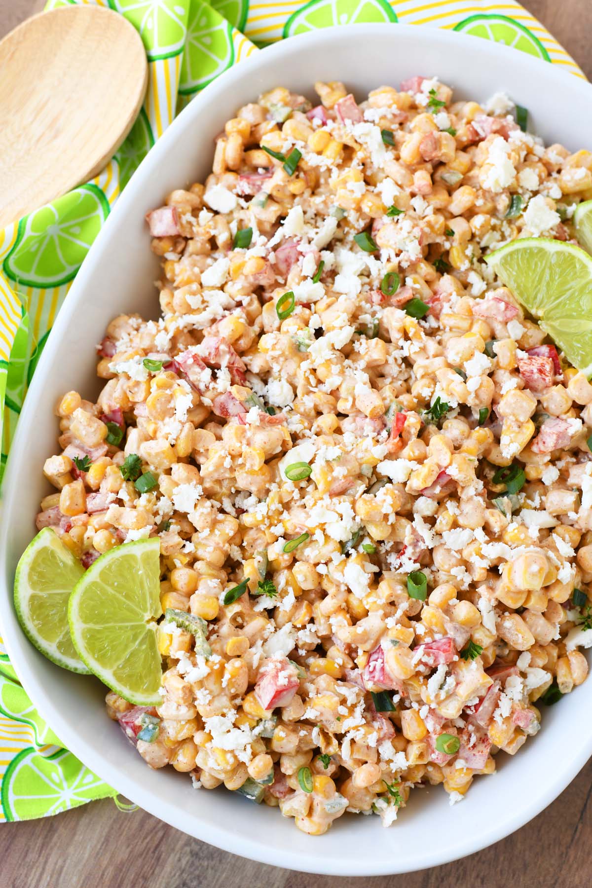 A white dish of corn salad with lime wedges near a lime napkin.