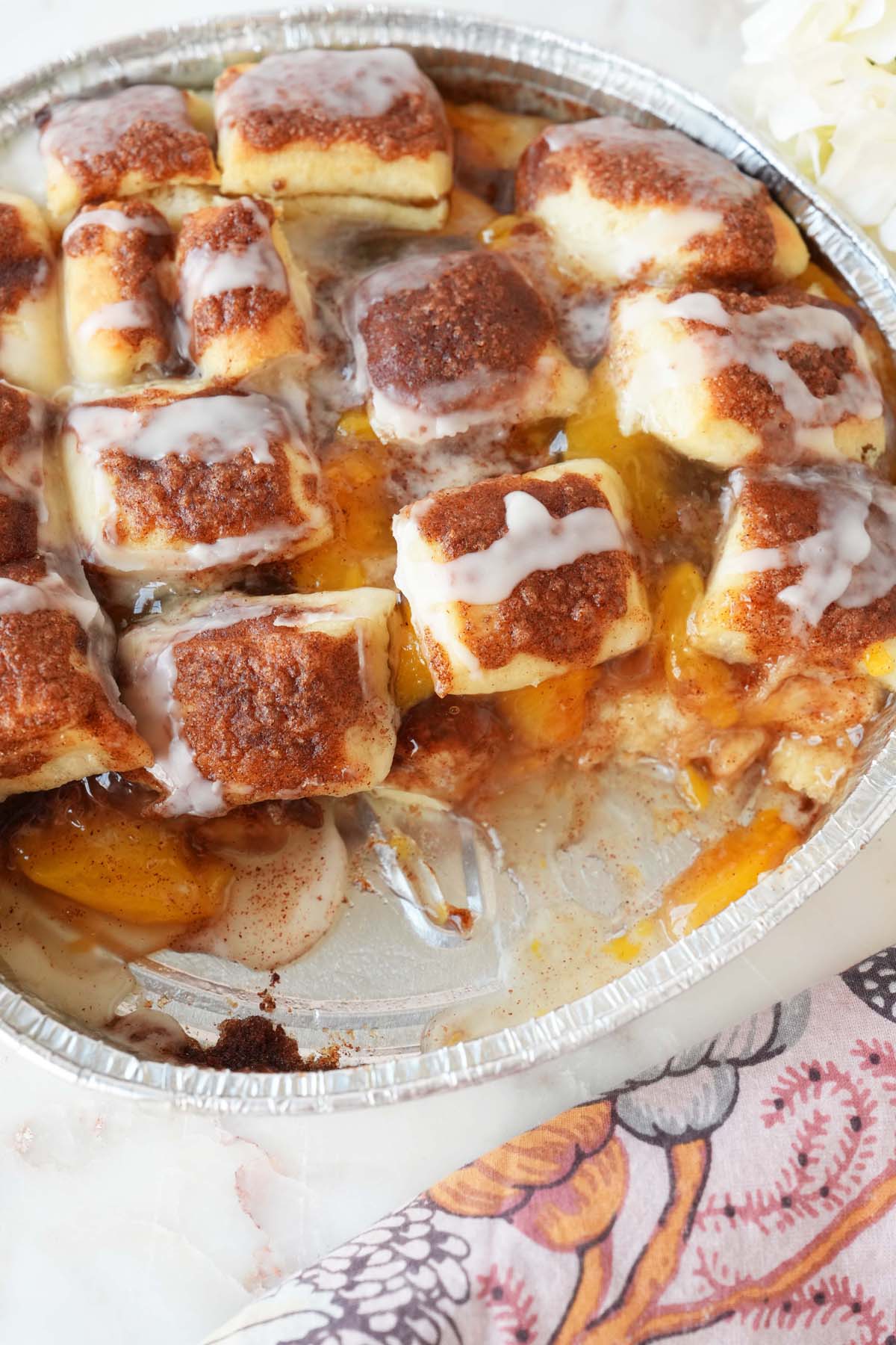 Peach cinnamon parker house rolls in a foil pan near a floral napkin.