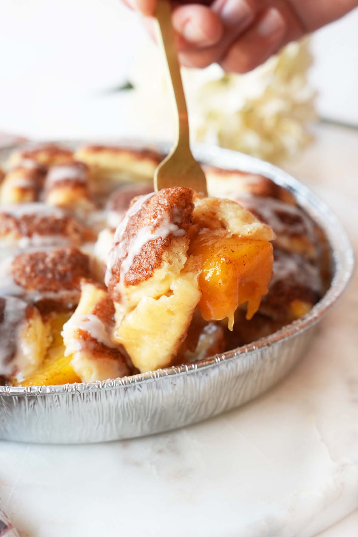 A hand holding a gold fork with peach bun cobbler on it.