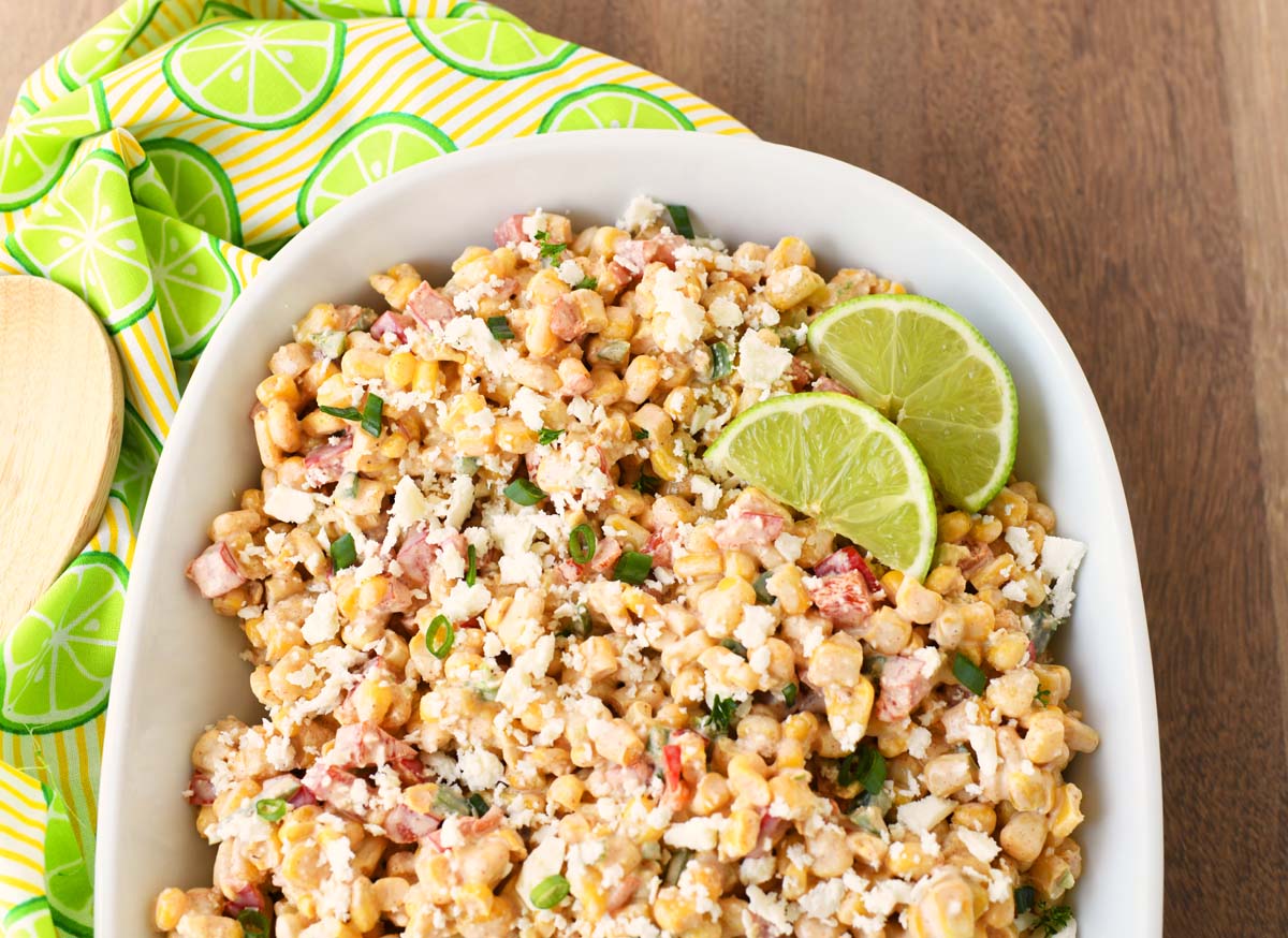 Lime wedges in corn salad on a wooden table with lime napkins.