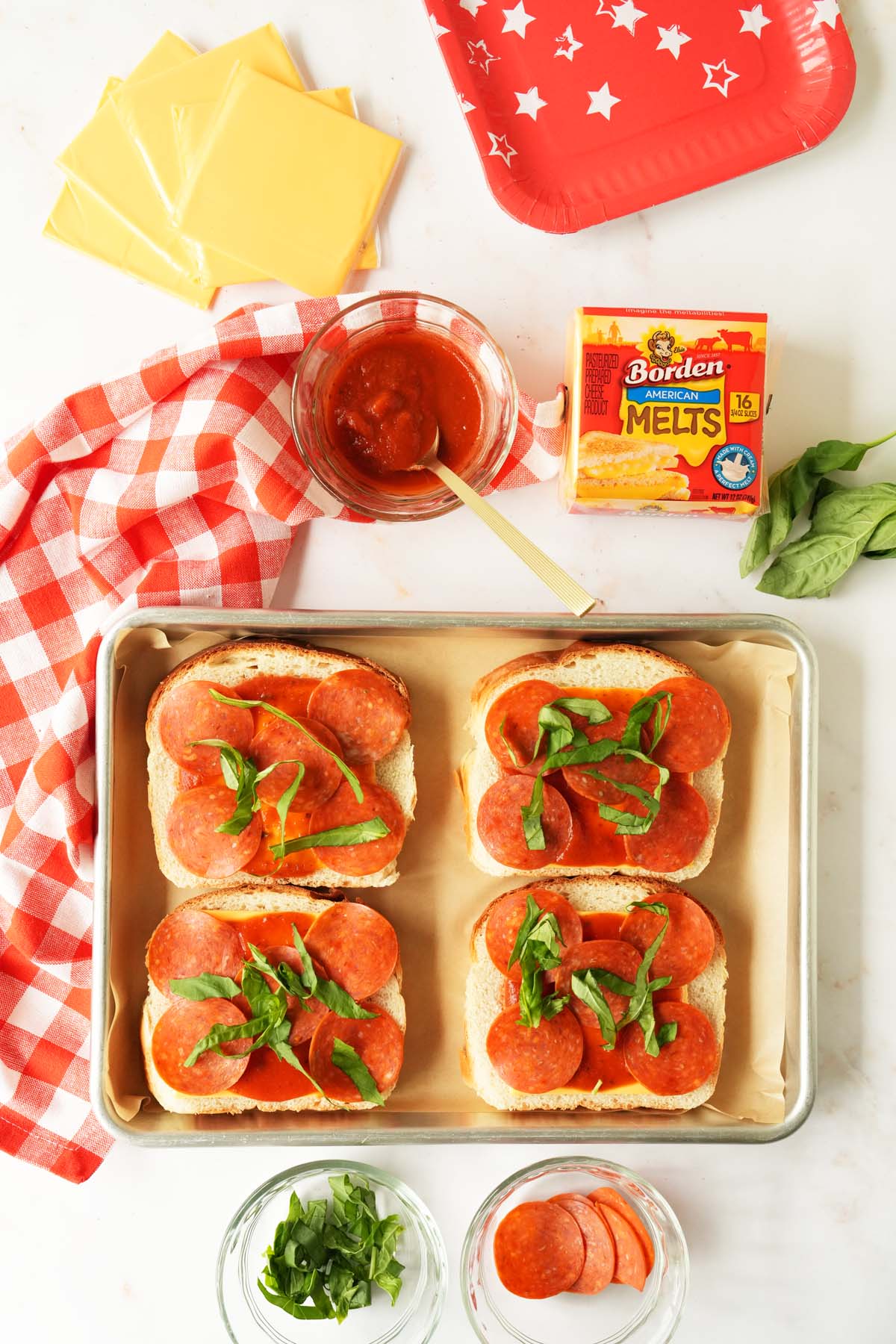 American bread on a parchment-lined baking sheet with sauce, pepperoni, and fresh basil.