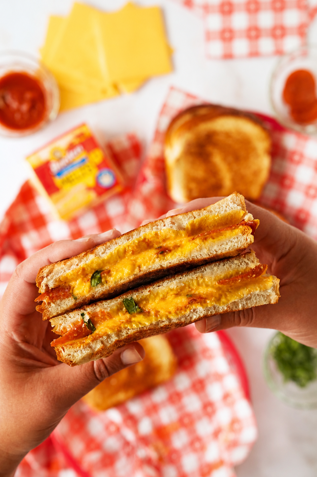 Tan hands holding up a grilled pepperoni and cheese sandwich that is cut in-half.