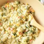 A spoon inside a tan bowl of Brazilian potato salad near a citrus napkin.