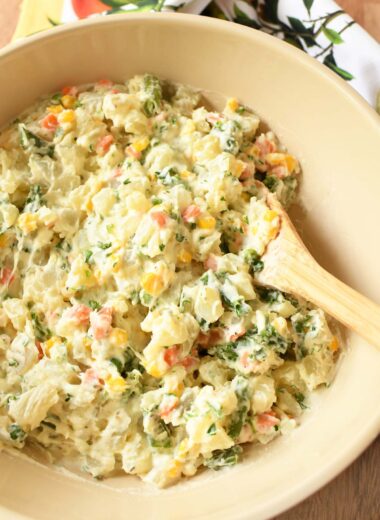A spoon inside a tan bowl of Brazilian potato salad near a citrus napkin.