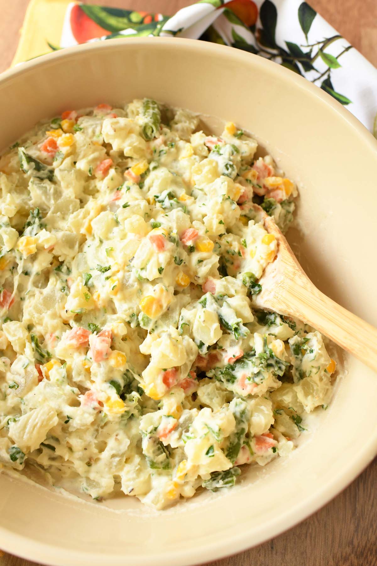 A spoon inside a tan bowl of Brazilian potato salad near a citrus napkin.