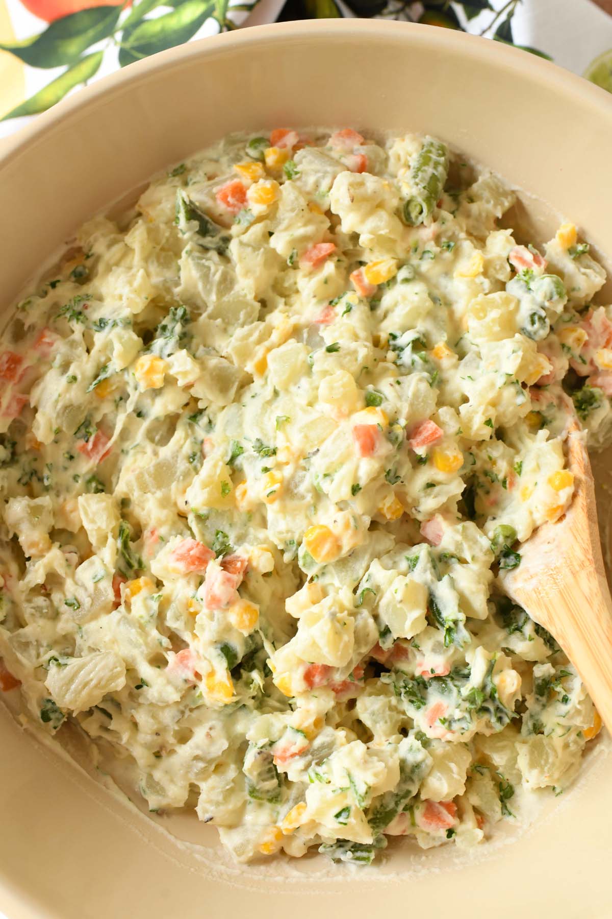 Up-close shot of Brazilian Potato salad in a tan bowl with a wooden spoon. 