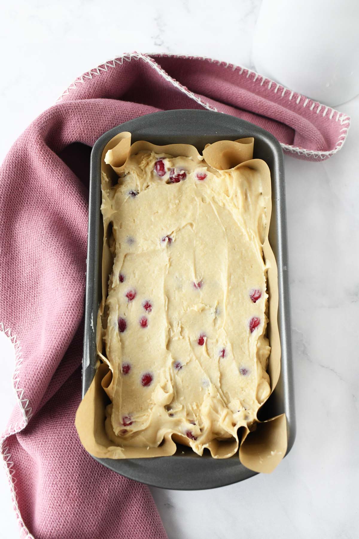 Cranberry loaf batter in baking pan near a pink napkin.