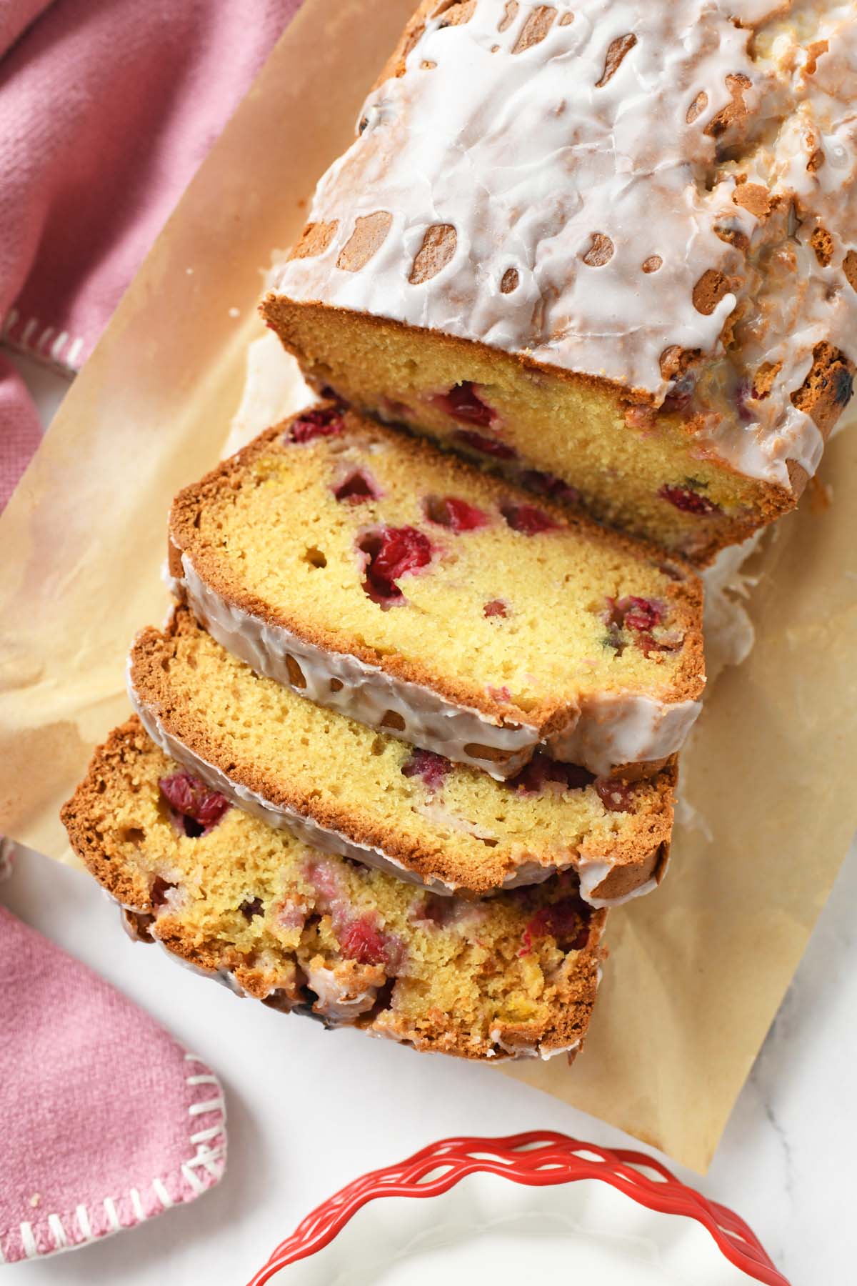 Sliced cranberry loaf near a pink napkin and red and white plates.
