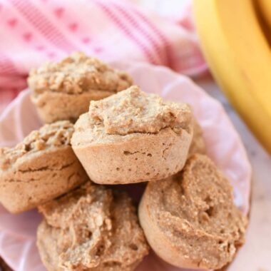Oatmeal banana muffins on a pink plate near a pink napkin and yellow banana.