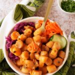 A gold fork resting inside a bowl of pickled, colorful veggies and rice topped with orange gochujang scallops.