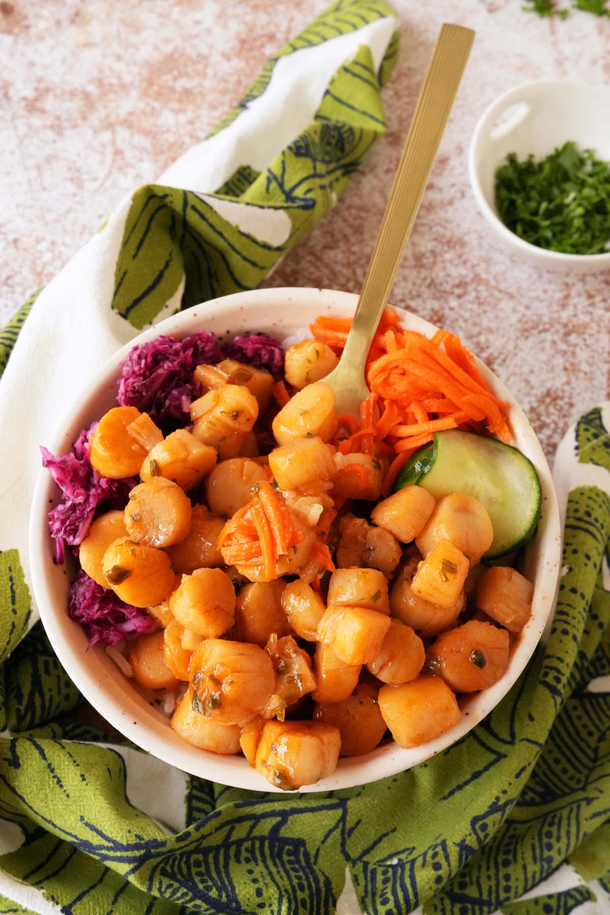 A gold fork resting inside a bowl of pickled, colorful veggies and rice topped with orange gochujang scallops.
