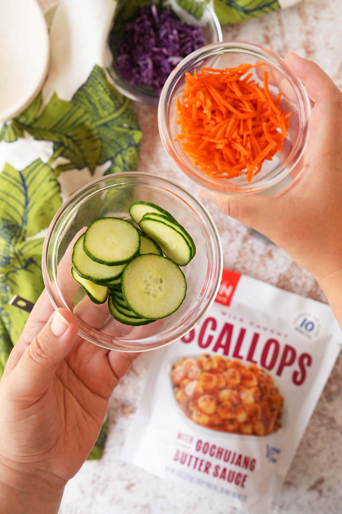 Hands holding up pickled cucumber and shredded pickled carrots.