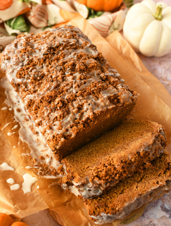 A sliced pumpkin crumb cake bread on neutral parchment paper on a harvest-themed table.