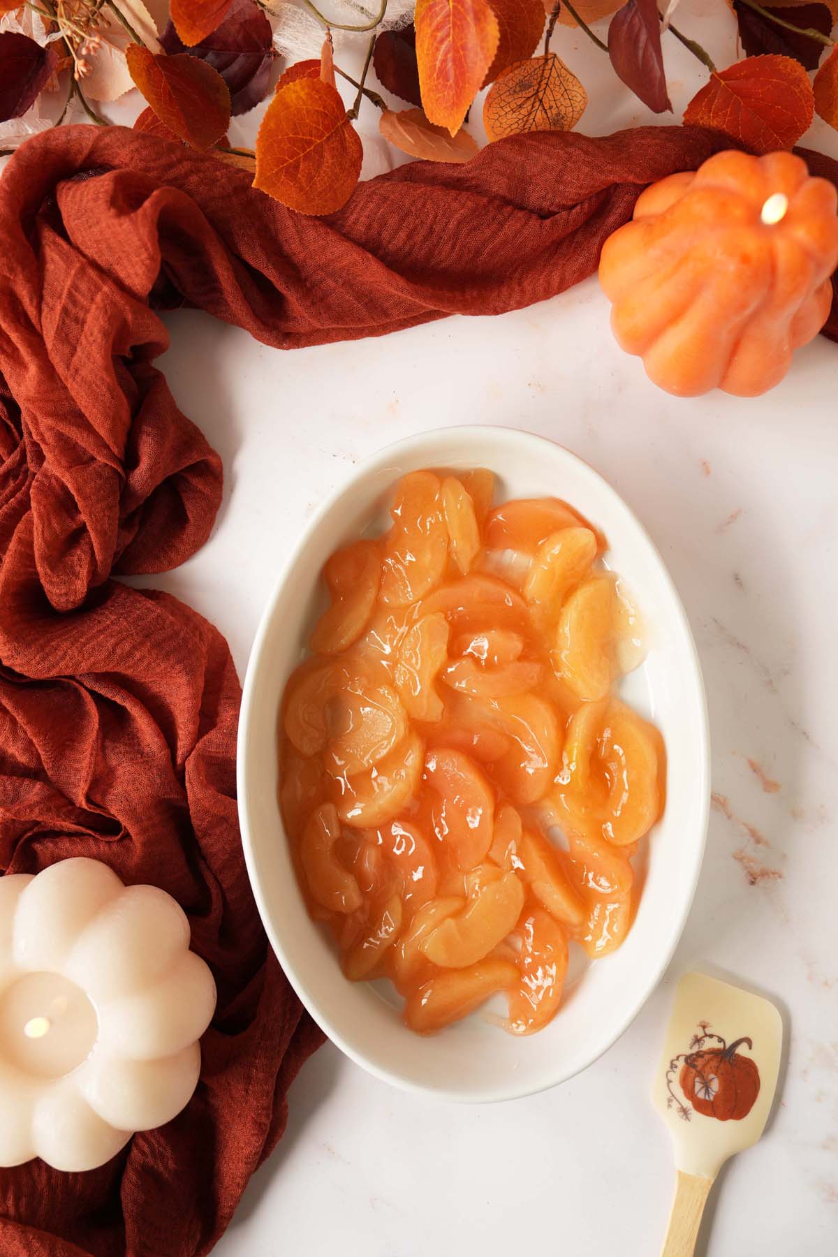 Canned apples in a white, oval baker on a fall-themed table.