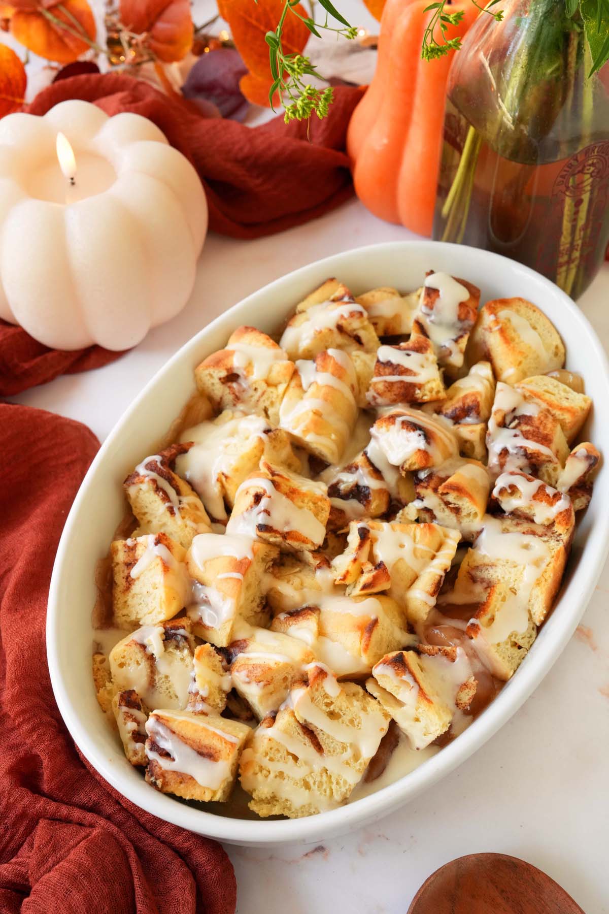 A baked white dish of apple cinnamon roll casserole on a fall-themed table.