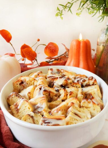 A comforting bowl of apple cinnamon casserole with fall candles and florals in the background.