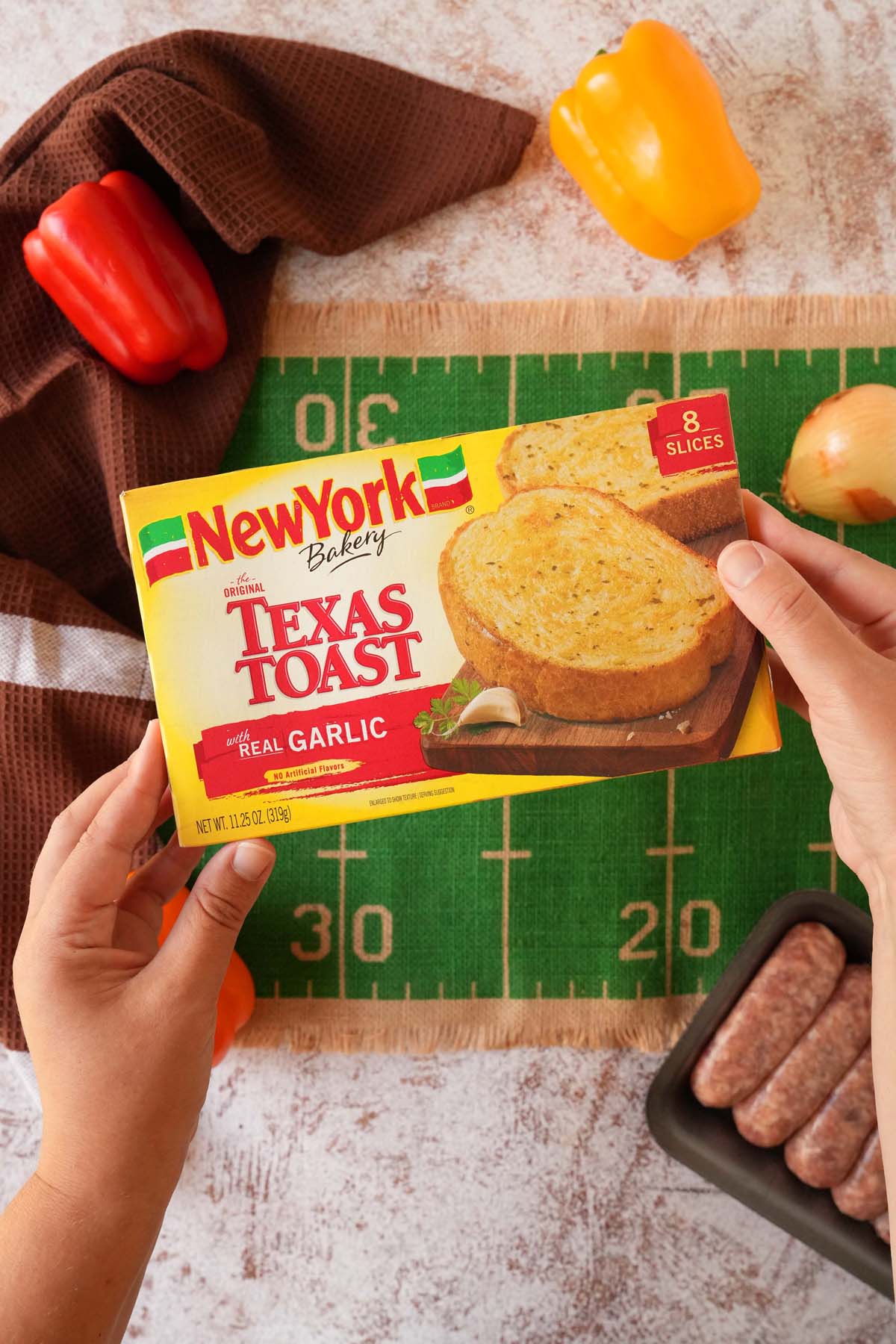 A hand holding a yellow box of New York Bakery Texas Toast near a football-themed table.