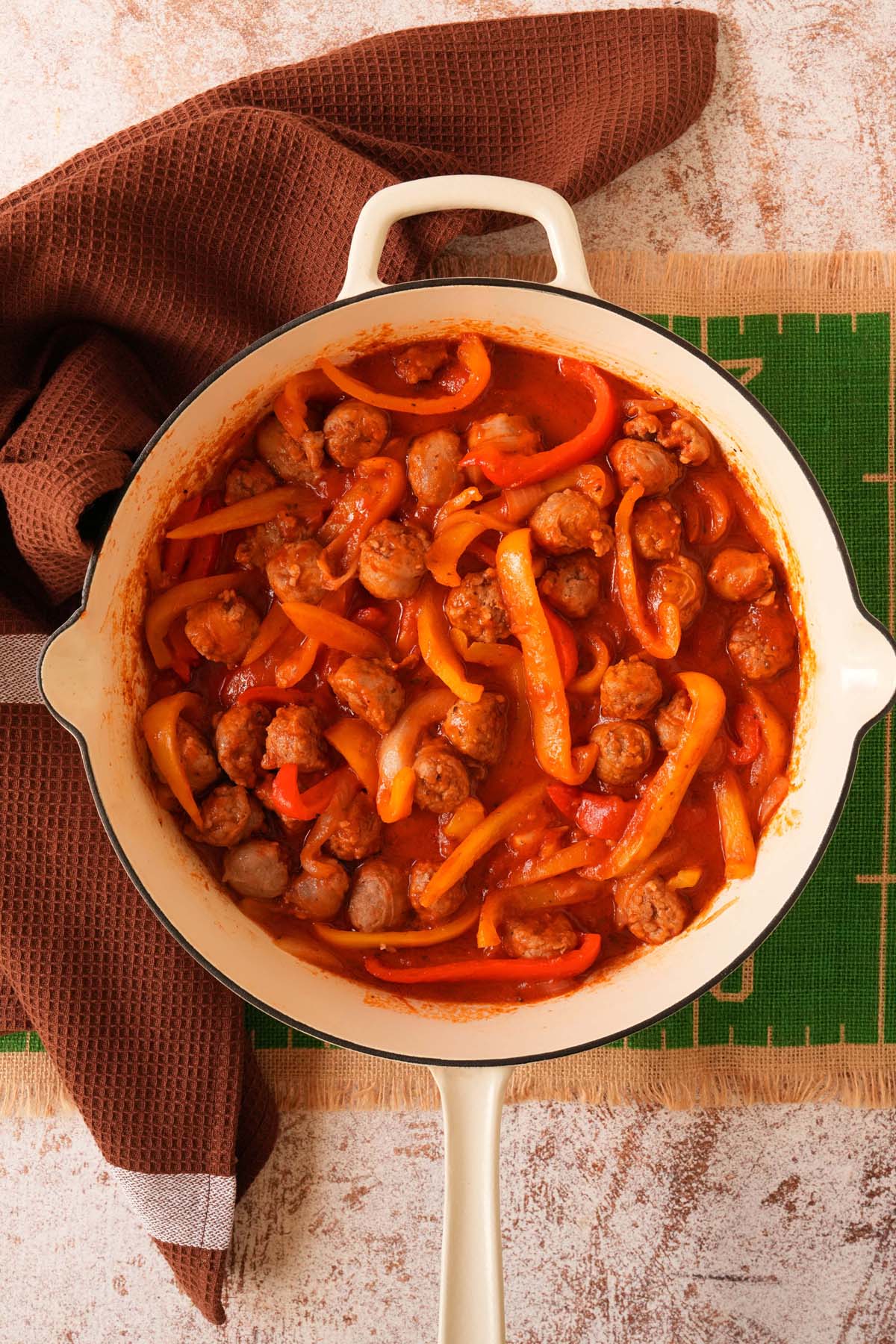 A white skillet filled wiht sausage and peppers resting on a football themed table.