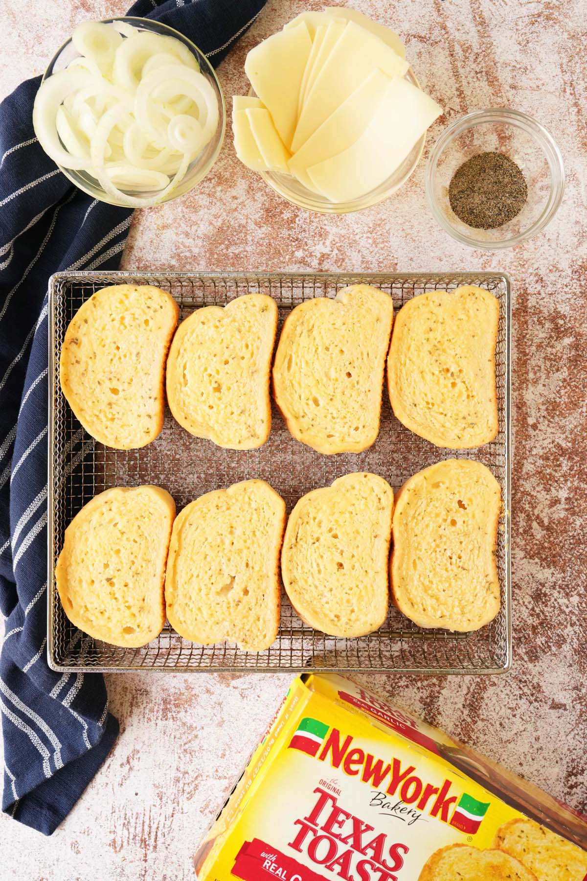 Texas Toast on an air fryer basket with ingredients and a blue napkin nearby.