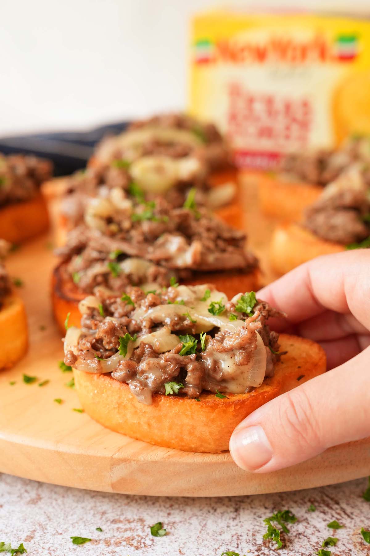 A hand holding a steak and cheese texas toast with parsley on top. A box of New York Bakery Toast is in the background.