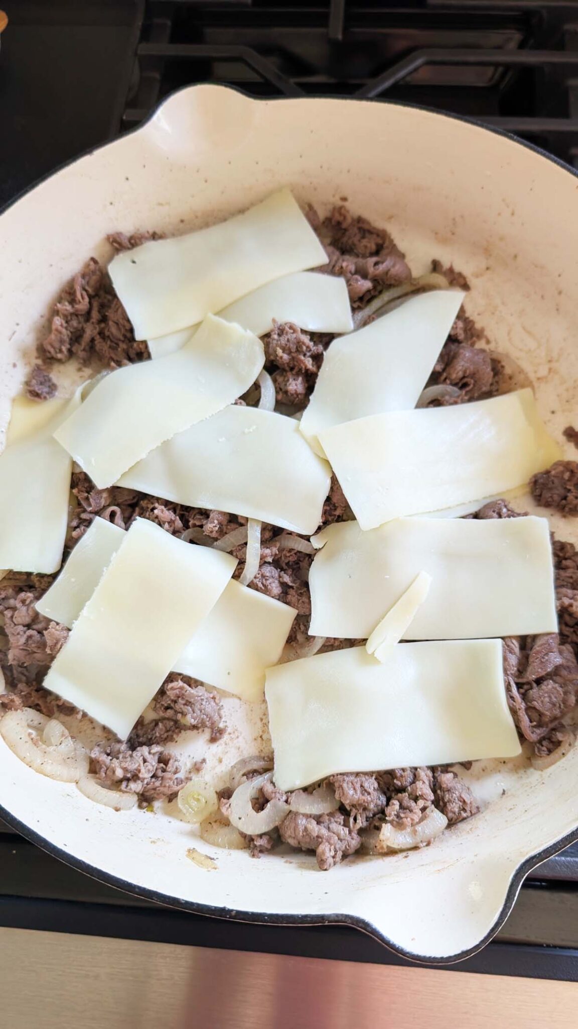 Cooked shaved steak in a white skillet with slices of American Cheese on top.