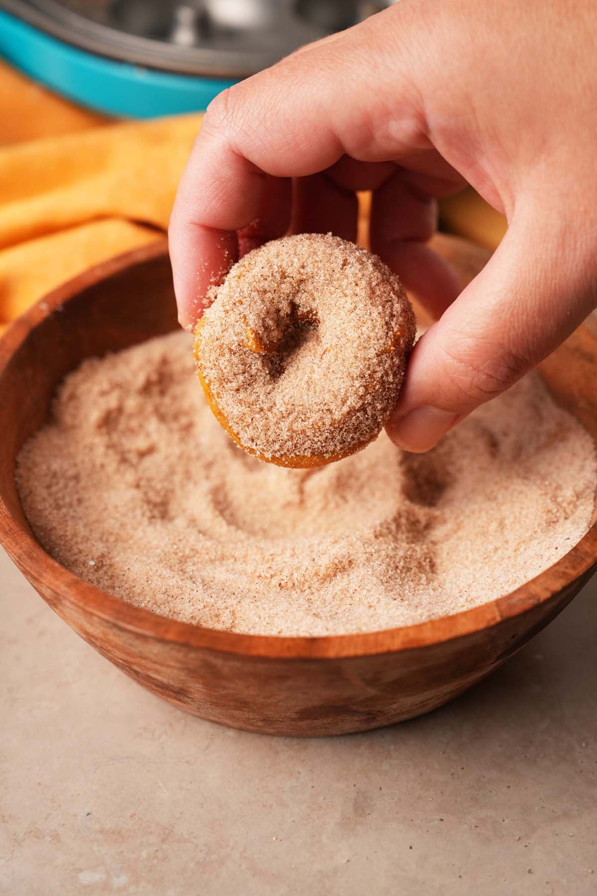 A hand dipping a pumpkin donut into cinnamon sugar.