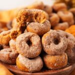 Up close shot of an opened pumpkin spice cinnamon and sugar donut in a woode bowl near an orange napkin.