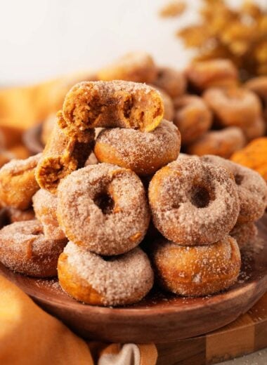 Up close shot of an opened pumpkin spice cinnamon and sugar donut in a woode bowl near an orange napkin.